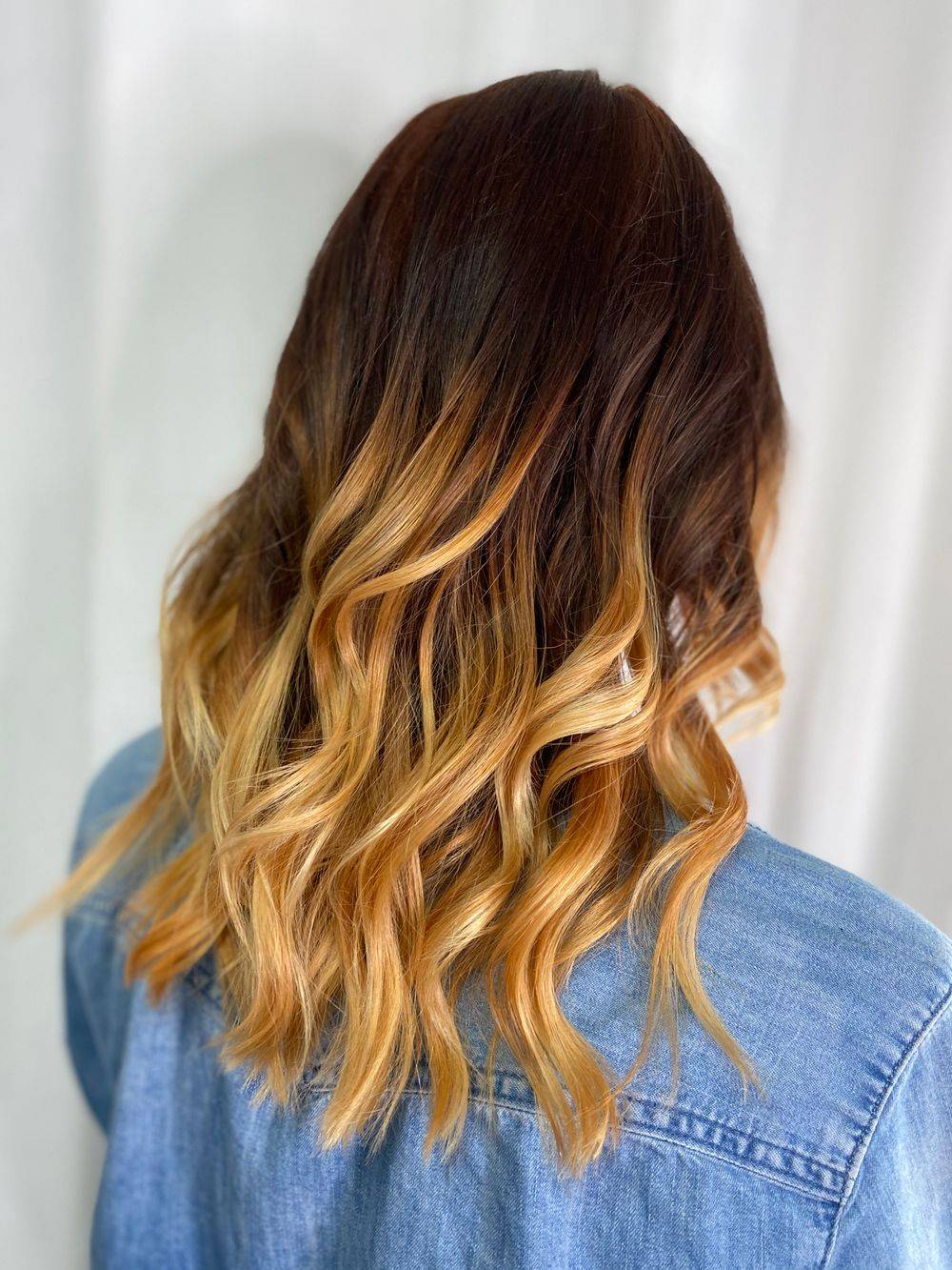 Long balayage hair melting from a dark espresso root to golden caramel ends
