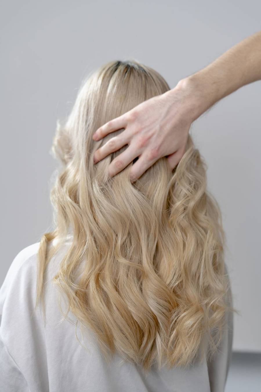 Stylist's hand lifting long, soft blonde curls